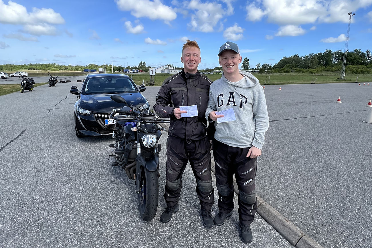 To motorcykel elever har bestået køreprøven og holder deres nye kørekort.